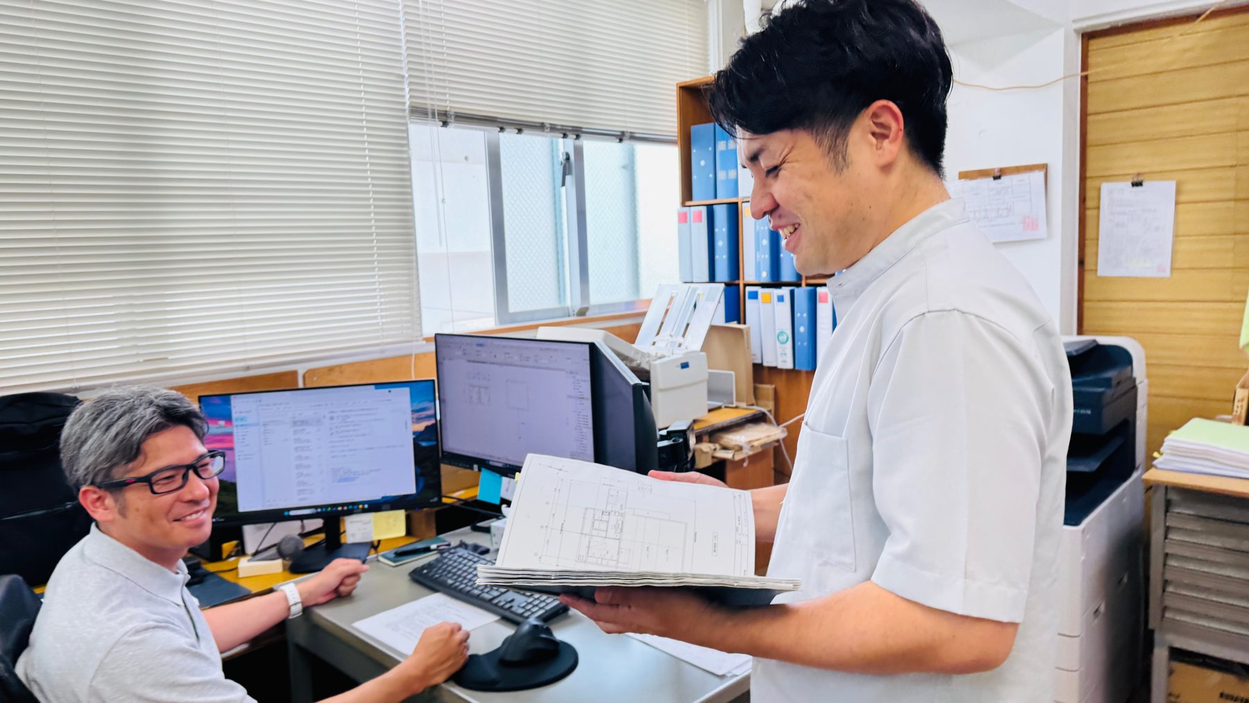 図面を手に、代表と先輩が笑顔で打ち合わせをする様子